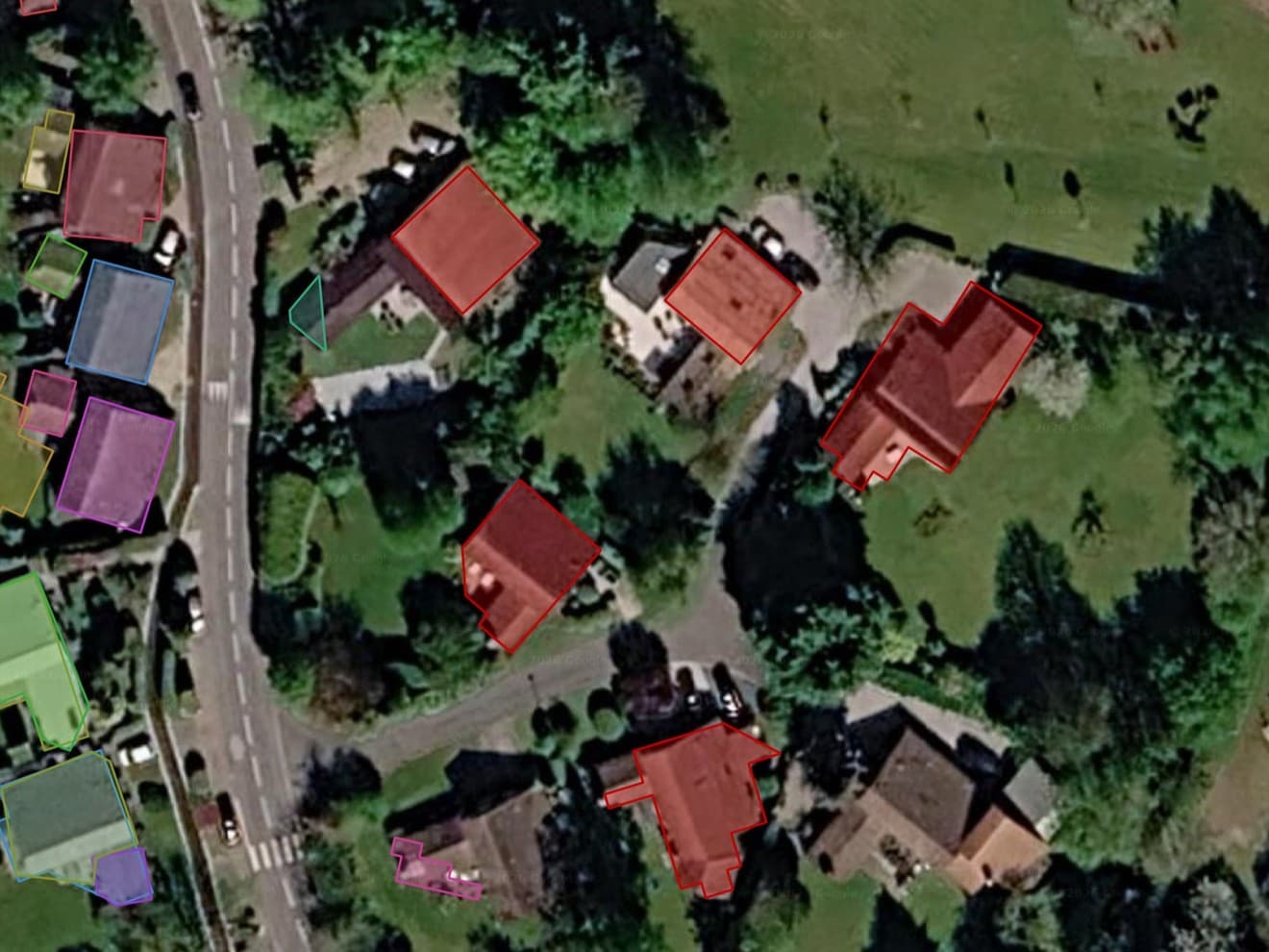 Vue satellite de la lisière d'un village, avec une route qui longe le côté gauche. La plupart des toits ont leur propre contour : cinq en rouge de l'autre côté de la route et une douzaine d'autres en bleu, vert, violet, orange et rose du côté proche. Deux maisons, un toit clair près du centre et un grand toit gris en bas à droite, n'ont aucun contour.