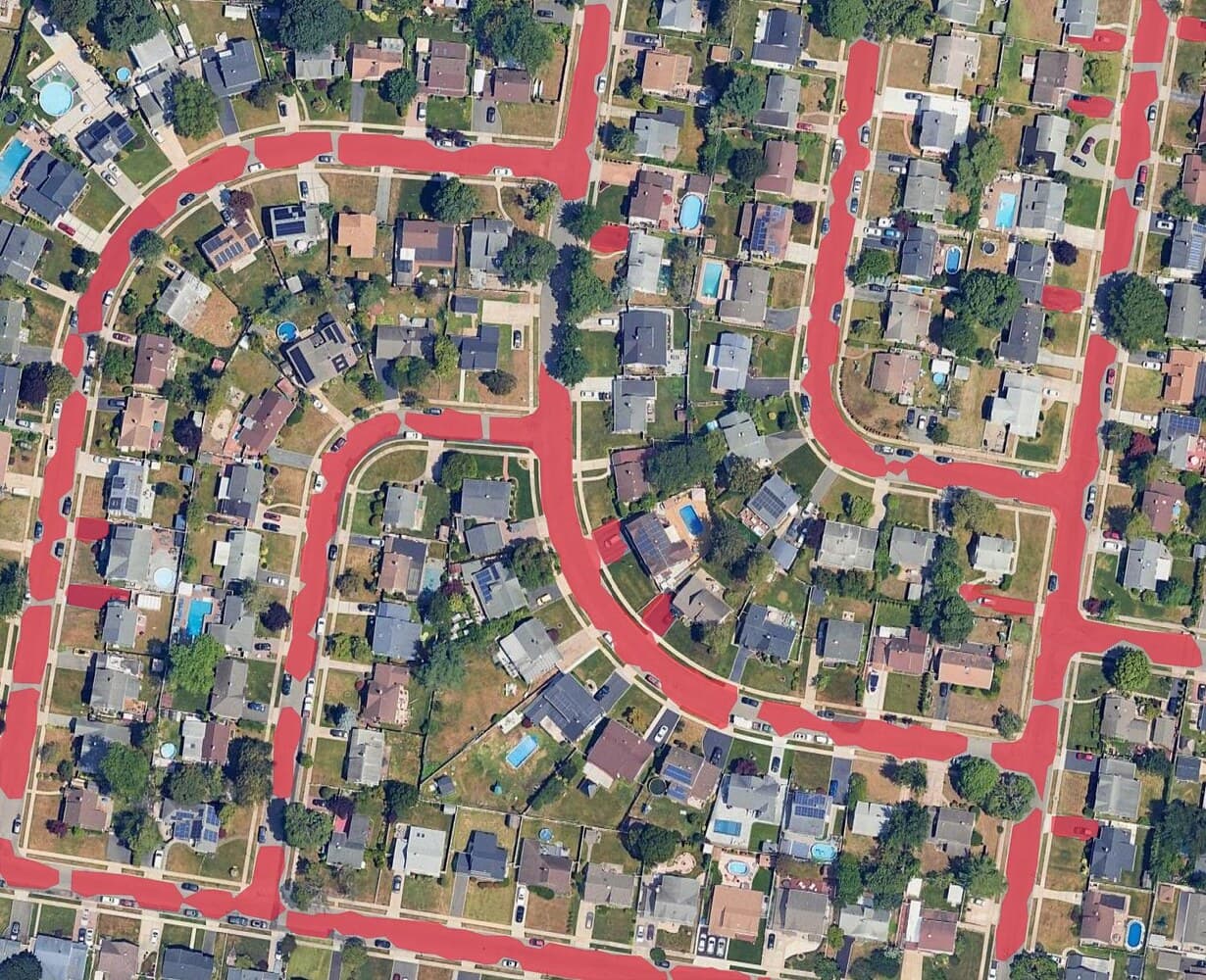 A suburban district on Google Satellite imagery in QGIS, the road surface filled kerb to kerb as one connected polygon layer in red.