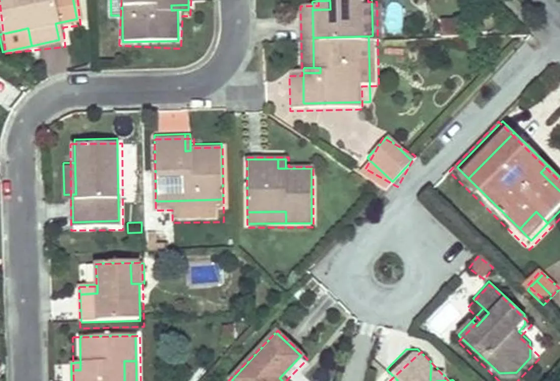 Luftbild freistehender Häuser mit Ziegeldächern in Saint-Jean bei Toulouse. Ein durchgezogener grüner Umriss, der Wandumriss des Katasters, liegt innerhalb jedes Dachs. Ein gestrichelter roter Umriss, das Machine-Learning-Polygon von Microsoft, folgt der äußeren Dachkante und umschließt bei jedem Haus mehr Boden.