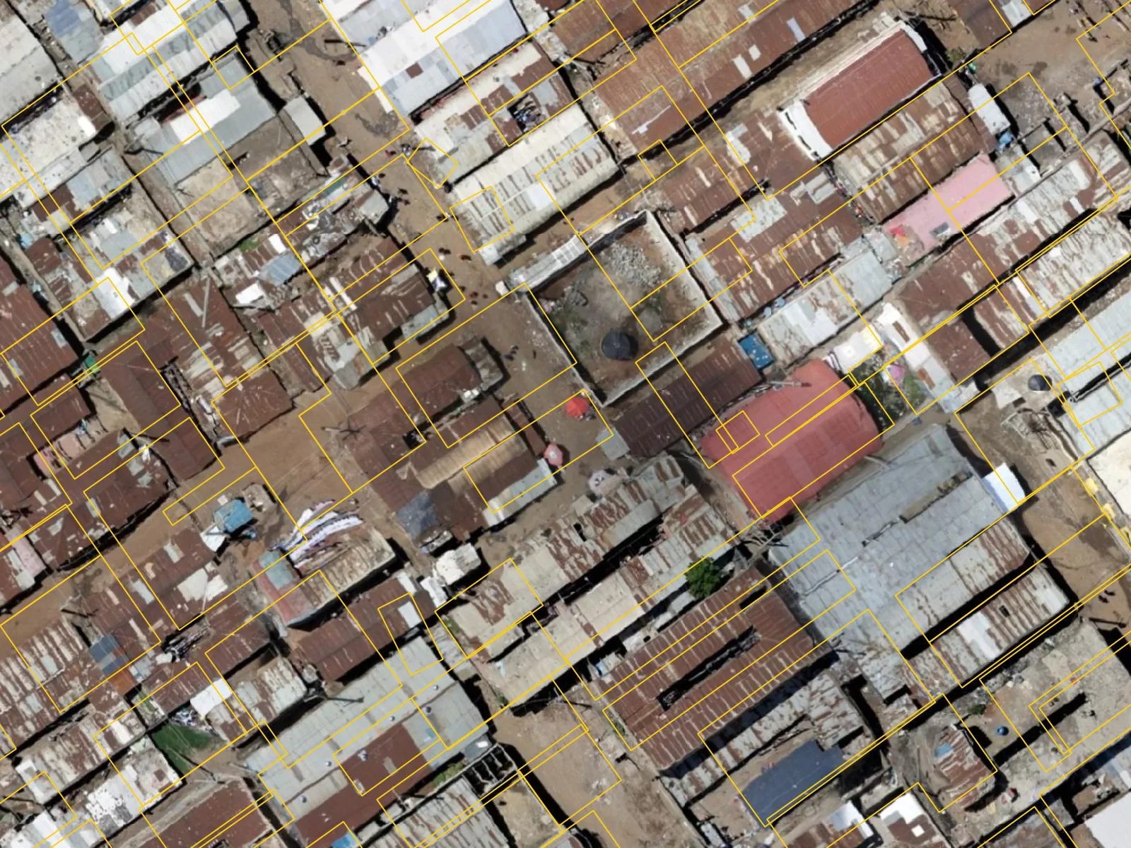 A dense block of tin roofs in Dandora, Nairobi. Yellow Google rectangles form a regular grid that crosses roof edges and paths; blue OpenStreetMap outlines follow each cluster of roofs around its courtyard. (before)