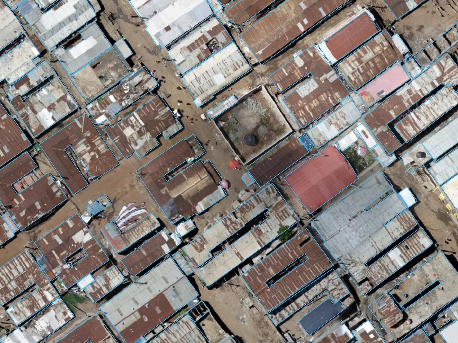 A dense block of tin roofs in Dandora, Nairobi. Yellow Google rectangles form a regular grid that crosses roof edges and paths; blue OpenStreetMap outlines follow each cluster of roofs around its courtyard. (after)