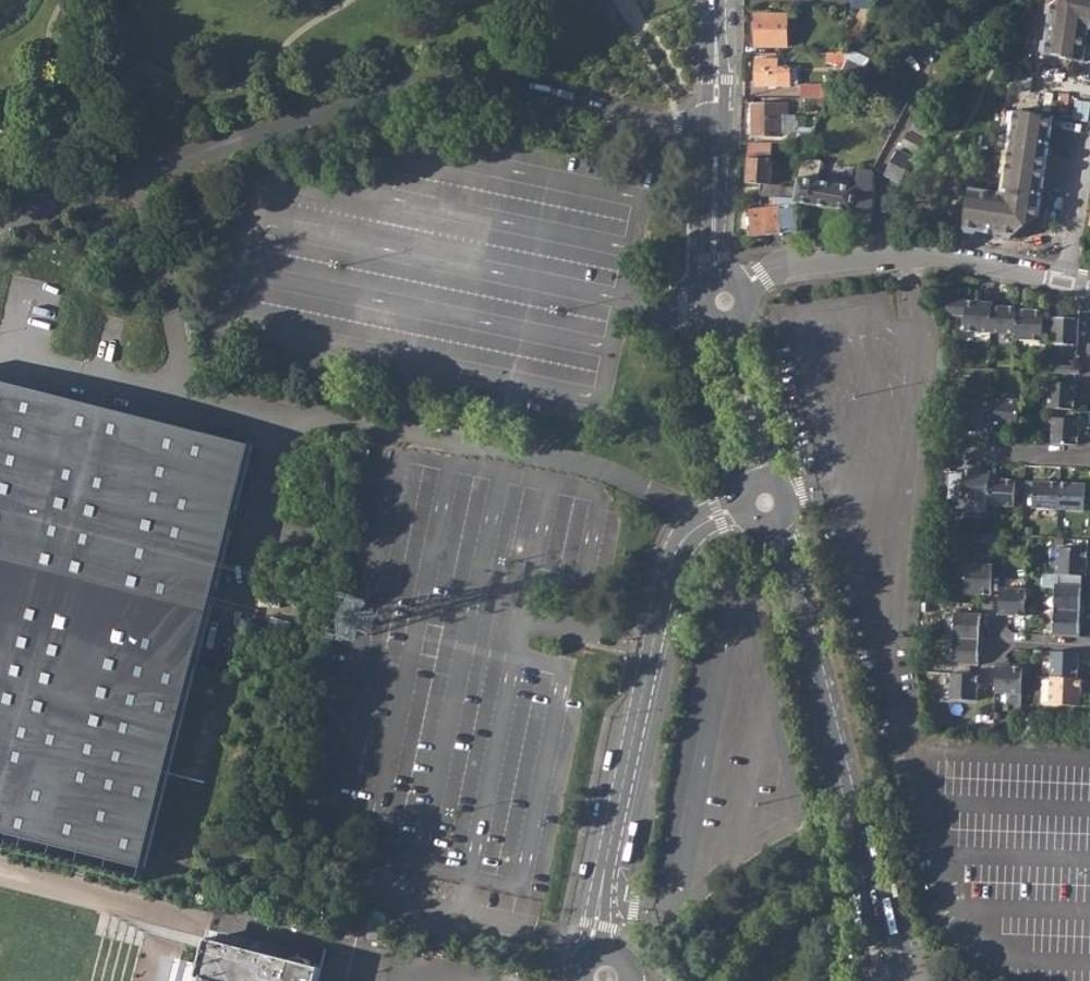The same aerial view redrawn as a flat site plan with white footprints, grey roads and pale green vegetation (before)