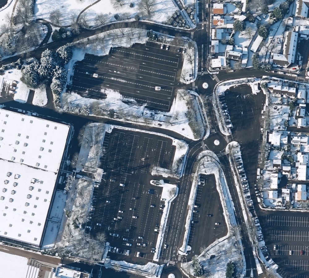 The same aerial view in winter with snow on roofs, lawns and canopies and wet cleared roads (after)